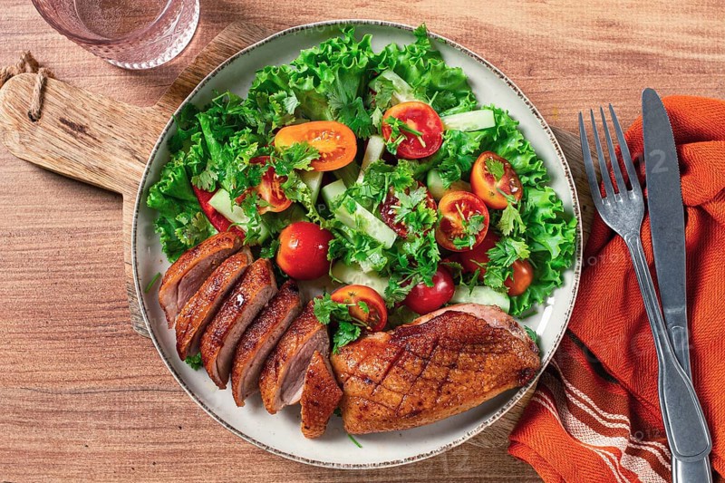 Delicious grilled duck breast served with fresh garden salad and cherry tomatoes at a rustic dining table