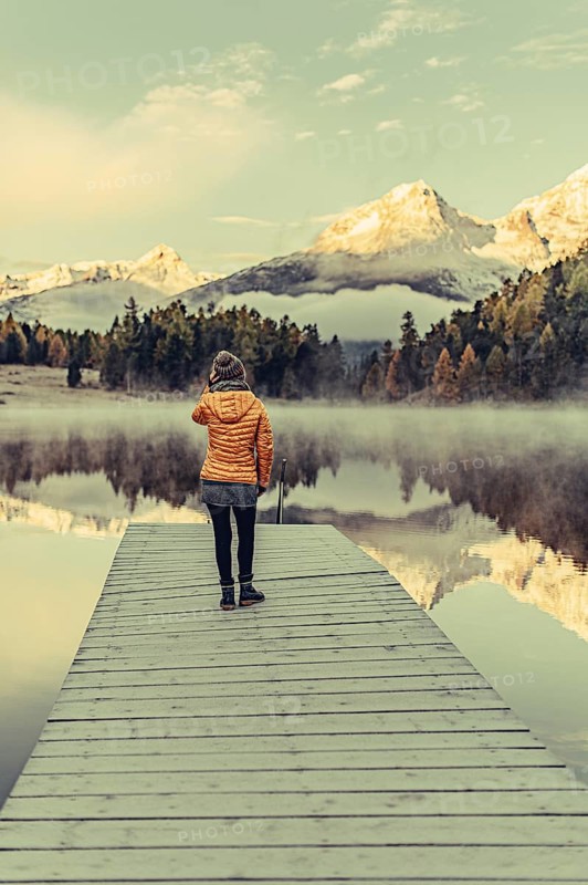 Young woman at Lake Staz near Sankt Moritz in the Engadine in Switzerland. Morning atmosphere with fog in autumn. Reflection of water