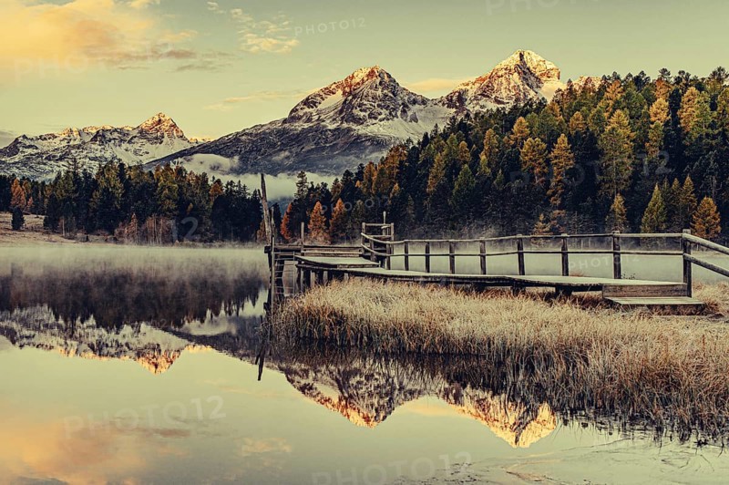 Lake Staz near Sankt Moritz in the Engadin in Switzerland. Morning atmosphere with fog in autumn. Water reflection and snow-covered mountains in the background