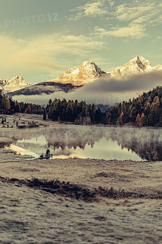 Lake Staz near Sankt Moritz in the Engadin in Switzerland. Morning atmosphere with fog in autumn. Water reflection and snow-covered mountains in the background