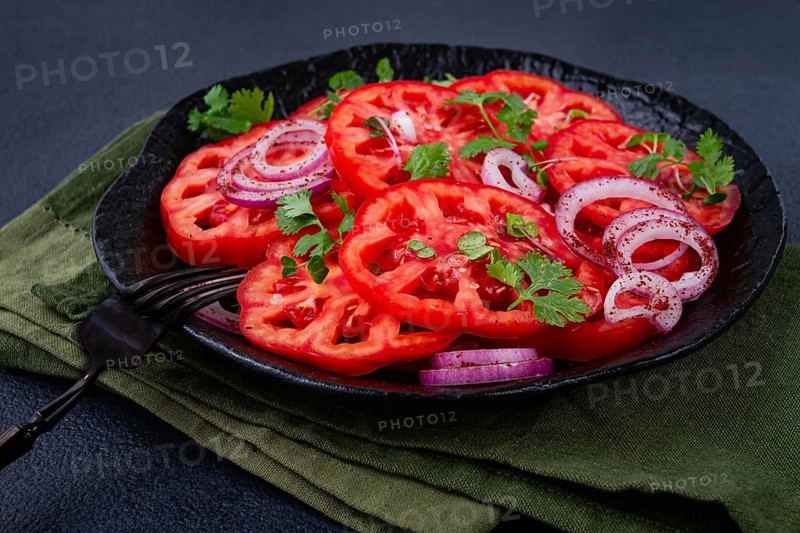 Freshly sliced tomatoes and red onions, garnished with herbs, on a black plate, summer salad, no people