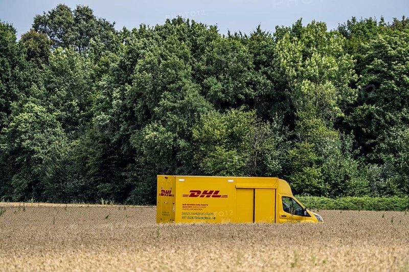 DHL parcel van, electric vehicle, on the way to a customer, rural, driving along a dirt track through a corn field, North Rhine-Westphalia, Germany