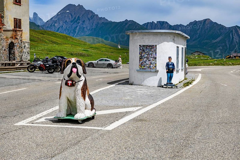 Disused former border hut for passport control at the border crossing between France and Italy, in the foreground figure of a St Bernard dog with a barrel around its neck, behind it figure of a French border official, Graian Alps, Département Savoie, France, Valle d'Aosta, Italy