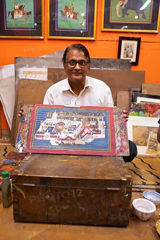 Miniature painter, 50 years old, shows a picture of the royal city palace in his studio, Udaipur, Rajasthan, India
