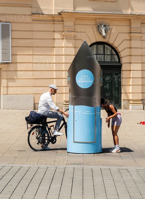 Two people in front of a drinking water fountain in the city centre of Vienna, Austria
