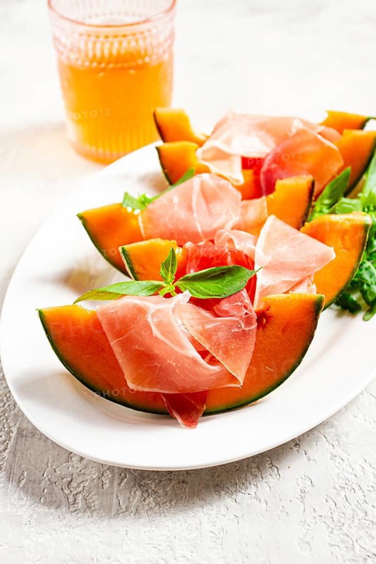 Cantaloupe melon with prosciutto and fresh basil, on a white plate, natural light