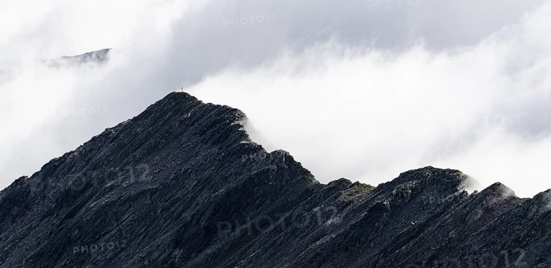 Mountain ridge with summit Zunderspitz and summit cross, cloudy, Stubai Alps, near Ridnaun, South Tyrol, Italy