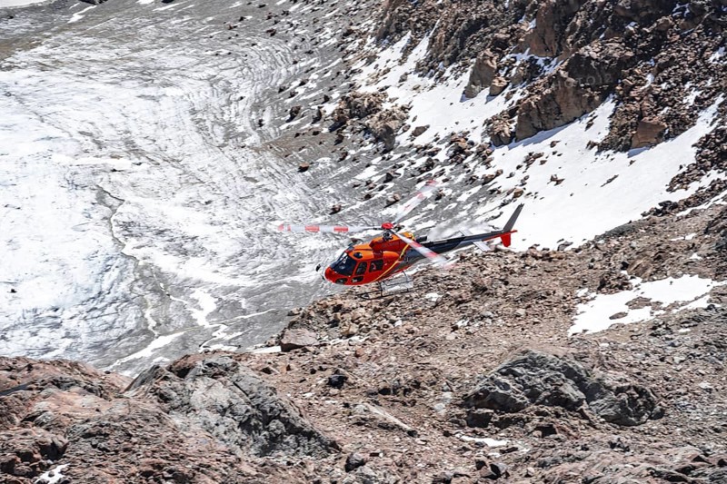 Red helicopter flies over glaciers in the mountains, Stubai Alps, South Tyrol, Italy