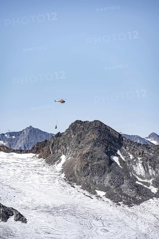 Helicopter with a load on a rope flies over glaciers and mountains, Stubai Alps, South Tyrol, Italy