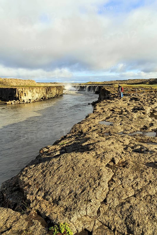 Hikers at the river Jökulsa a Fjöllum, canyon, waterfall Selfoss on the horizon, North Iceland, Iceland