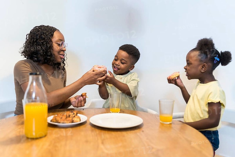 Happy family sharing a joyful breakfast at home, savoring delicious donuts and refreshing juice together in a warm kitchen setting