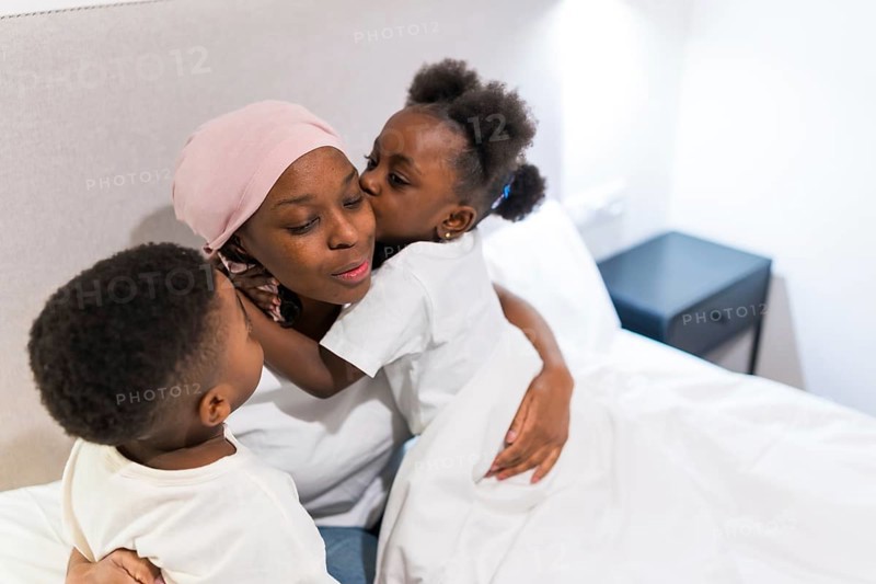 Two children hugging and kissing their sick mother in bed, showing support and love during cancer treatment