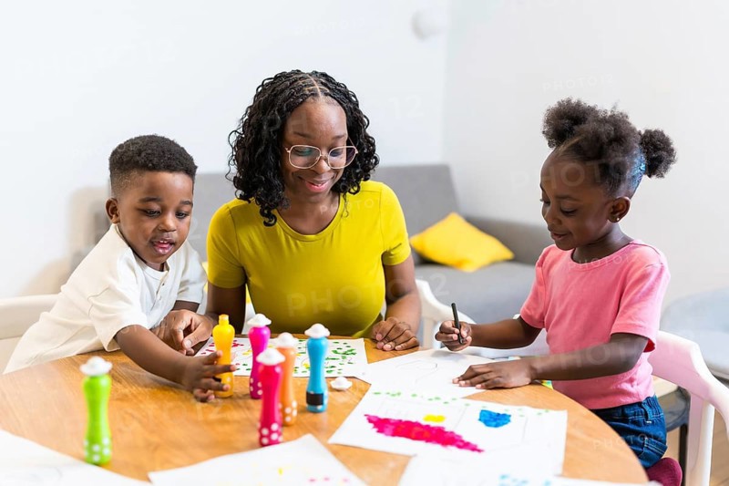 Mother and children enjoying creative playtime, using dot markers to create colorful artwork on paper at home, promoting family bonding and artistic expression