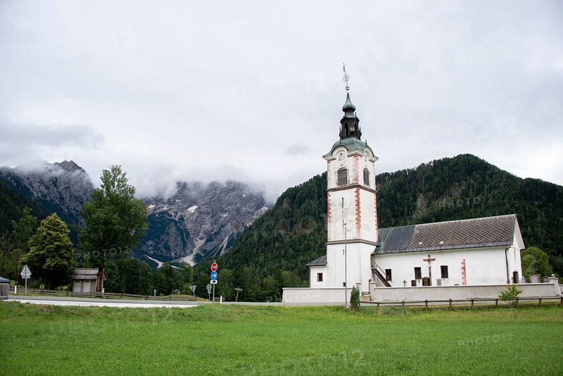 White church building against a mountainous background under a cloudy sky, Zgornje Jezersko, Gorenjska, Slovenia