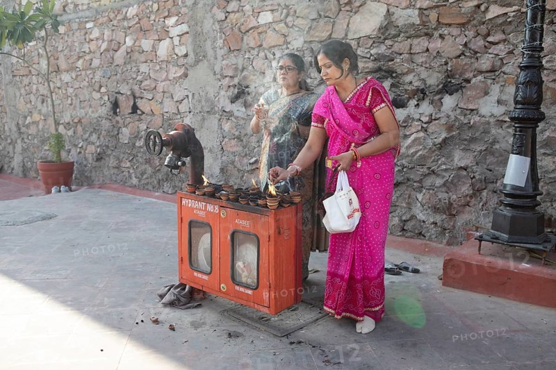 Indian woman lighting tea lights at a fire hydrant, Govind Dev Ji Hindu temple in the old city centre, Jaipur, Rajasthan, India