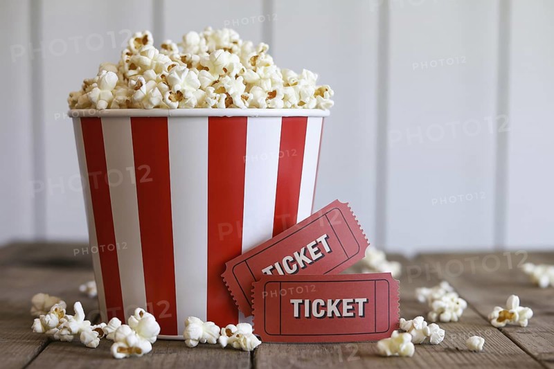 Red and white striped popcorn bucket with antique red movie tickets on rustic wooden table. Generative AI, AI generated