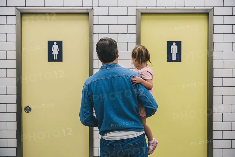 Father with young daughter hesitating in front of men's and women's restroom doors. Concept of gendered public toilet challenges for parents. Generative ai, AI generated
