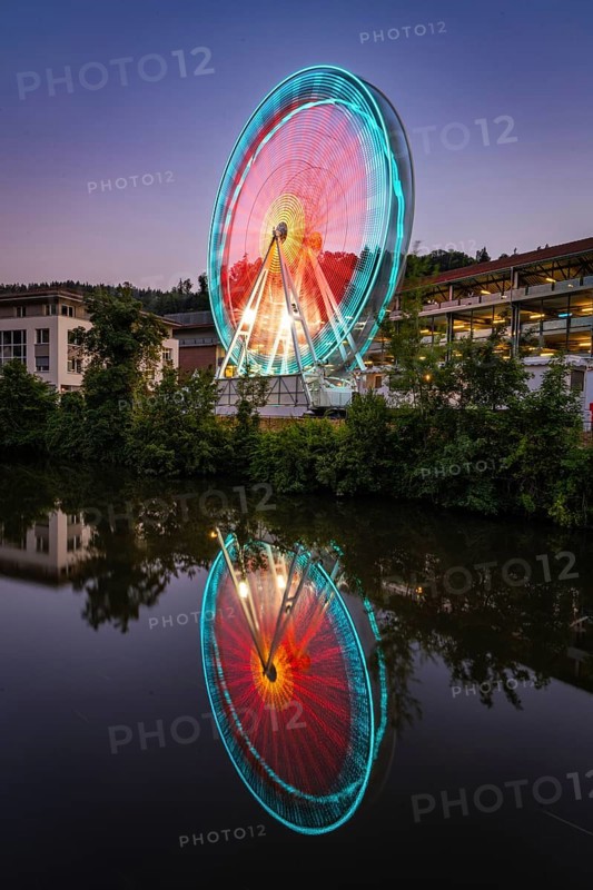 Illuminated Ferris wheel at night reflected in the water, in shades of blue and red, Calw, Germany