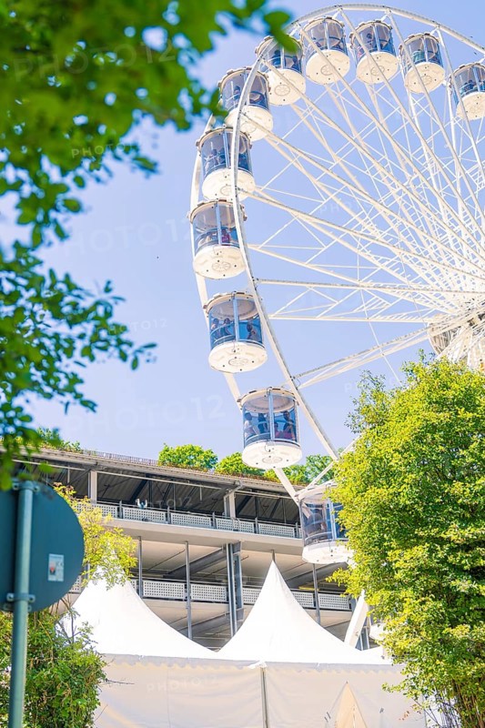 Ferris wheel and tents in an urban setting, framed by trees against a bright summer sky, Calw, Germany