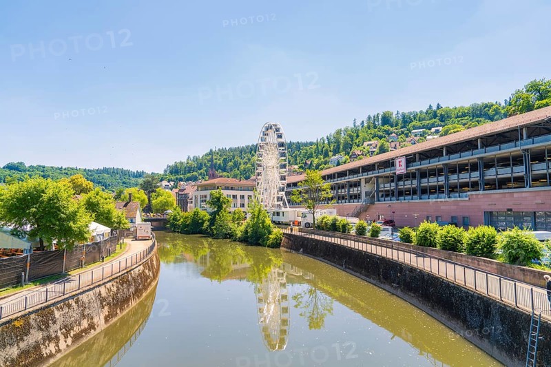 Urban surroundings with a Ferris wheel on the riverbank, wooded hills and clear summer air, Calw, Germany