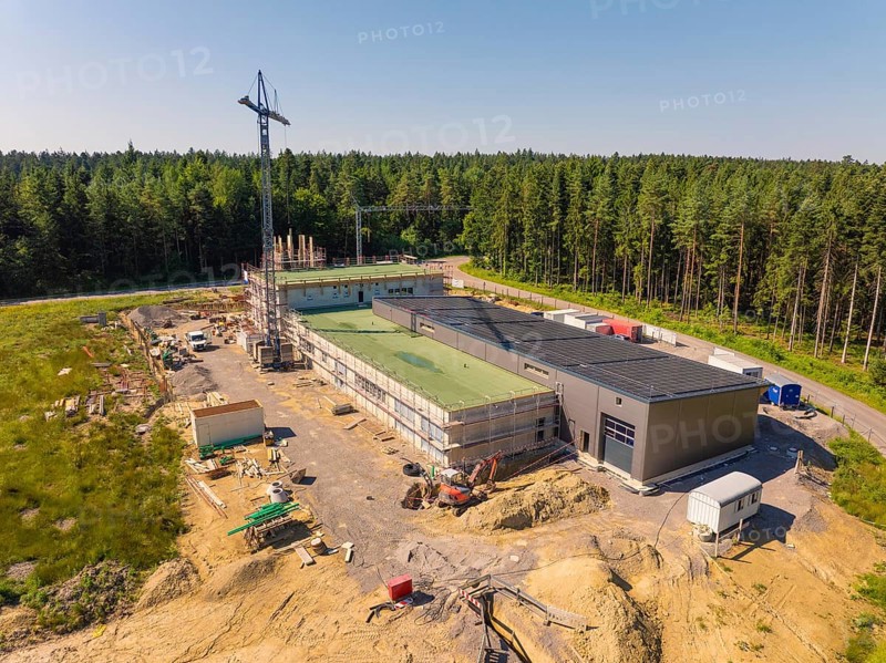 Outdoor construction site with solar roof and crane, surrounded by forest in sunny weather, new fire station, Oberhaugstett, district of Calw, Germany