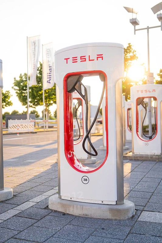 A Tesla charging station at sunset in an urban environment in front of green trees, Tesla Supercharger Böblingen, Germany