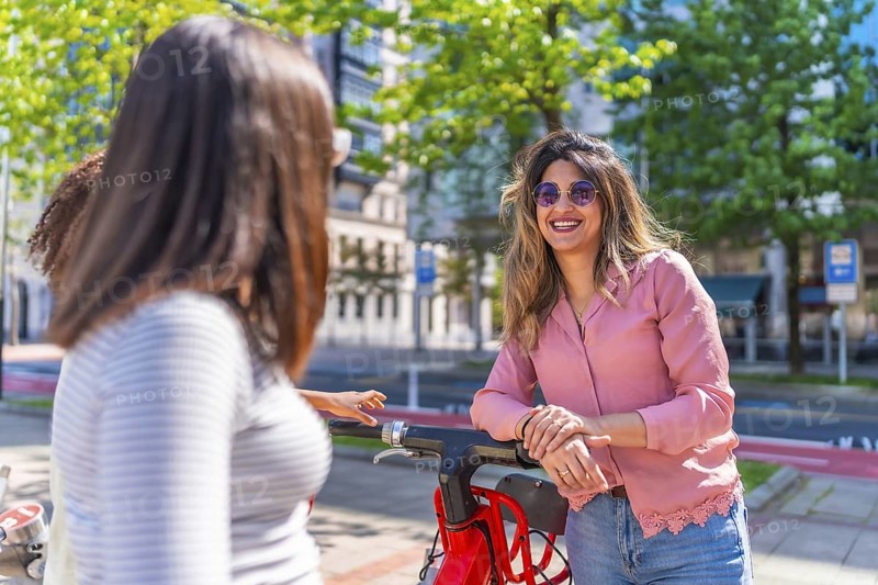 Group of friends talking and smiling next to a red electric scooter in a sunny summer day in the city