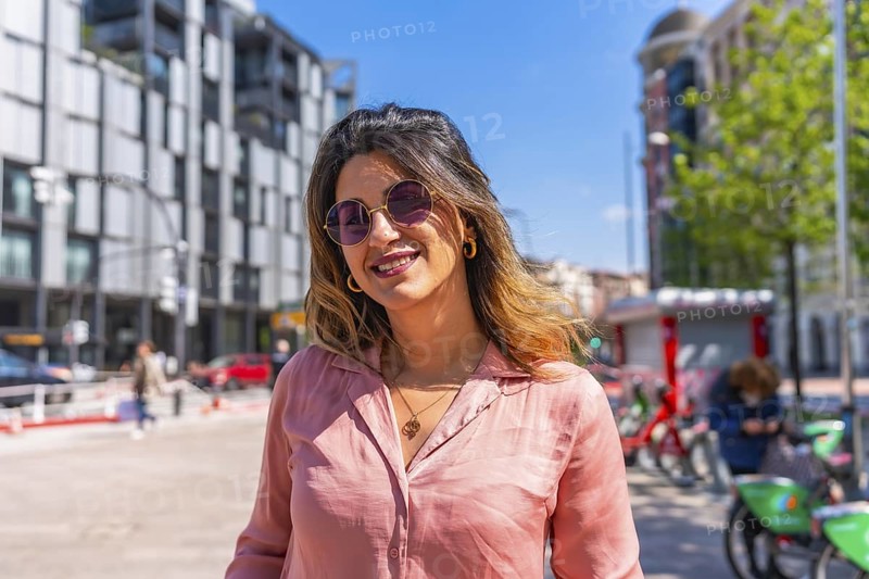 Portrait of a beautiful brunette woman smiling wearing sunglasses in a city on a sunny summer day