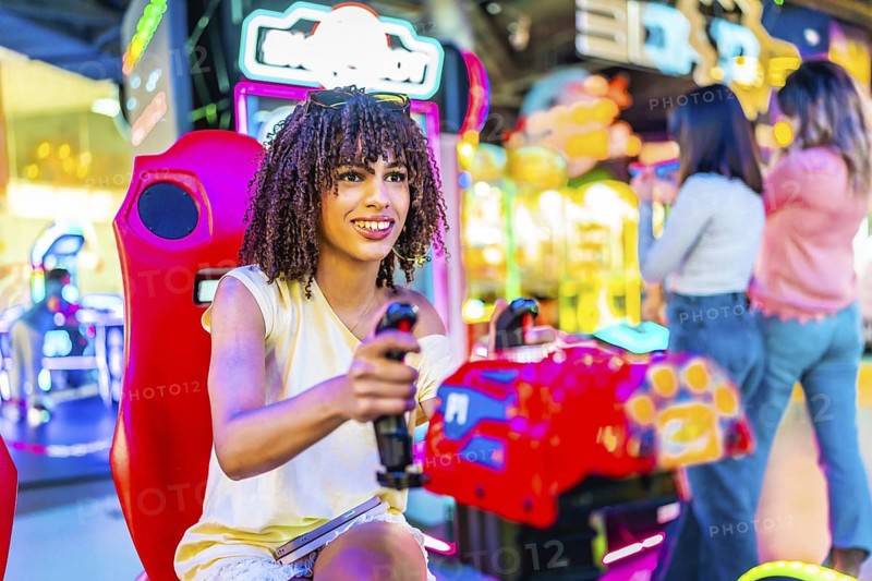 Young woman having fun playing a racing simulator in an amusement arcade with her friends in the background