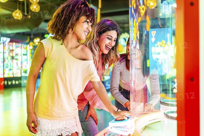 Three cheerful female friends enjoying their time together playing an arcade game in an amusement park