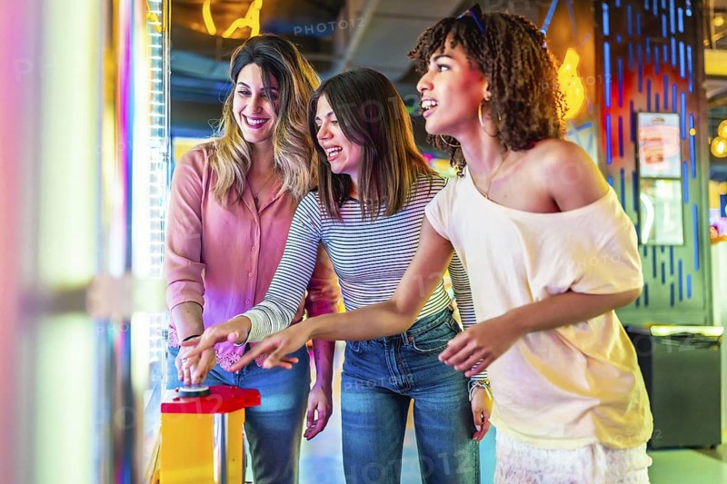 Three female friends enjoying a vibrant summer night out in the city, laughing and playing arcade games together, creating joyful memories