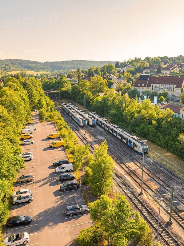 A train runs through a green landscape with trees and a car park, summer atmosphere, Weil der Stadt station, Böblingen district, Germany