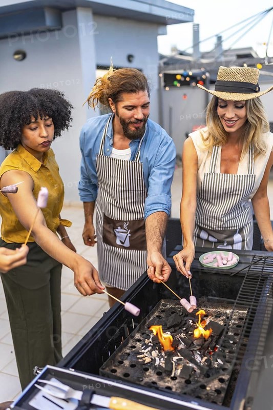 Cheerful friends enjoying a rooftop party, grilling marshmallows on skewers over a lively barbecue fire, creating fun summer memories together