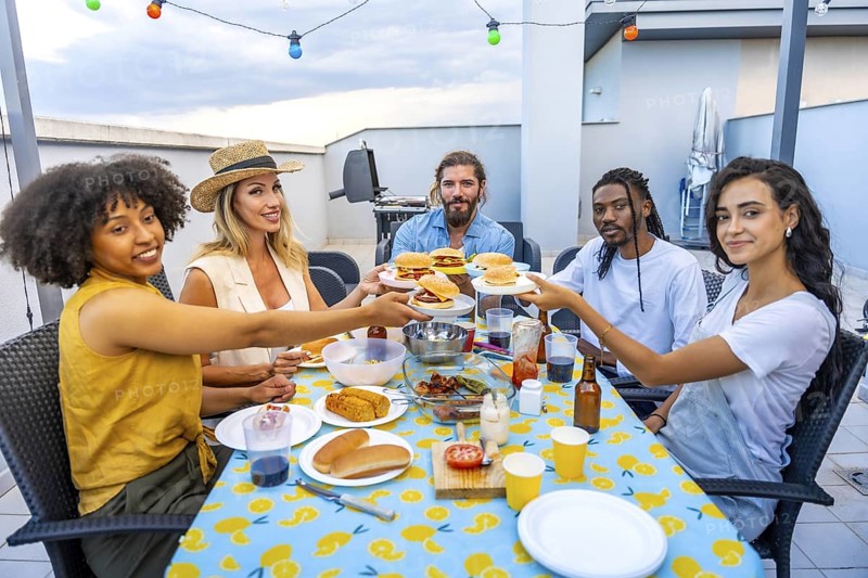 Diverse group of friends laughing and enjoying delicious burgers while celebrating summer at a lively rooftop barbecue party