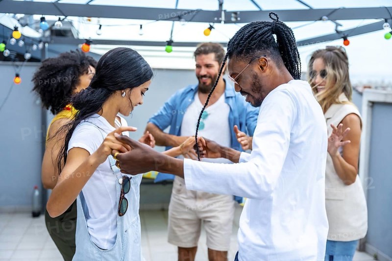 Young people dancing joyfully at a vibrant rooftop party, soaking in the summertime atmosphere and celebrating together under the evening lights