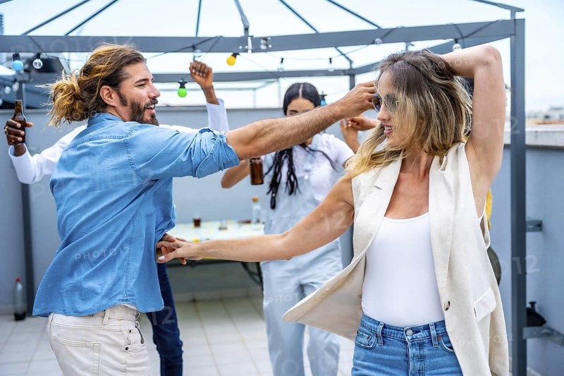 Cheerful young people dancing and having fun at a rooftop party, celebrating friendship and enjoying drinks