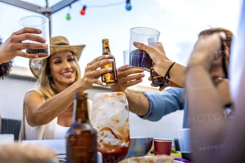 Cheerful friends raising glasses and bottles, making a toast during a rooftop party, celebrating their friendship with joy and excitement