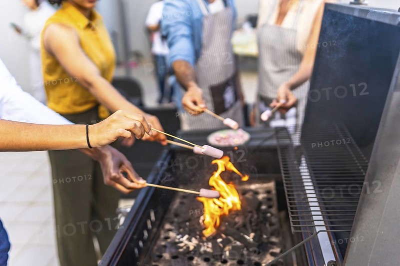 Friends are grilling marshmallows on skewers over a barbecue fire, enjoying a summer cookout together
