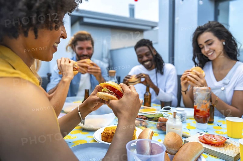 Cheerful multi ethnic friends savoring delicious burgers while enjoying a lively rooftop barbecue party filled with laughter and togetherness