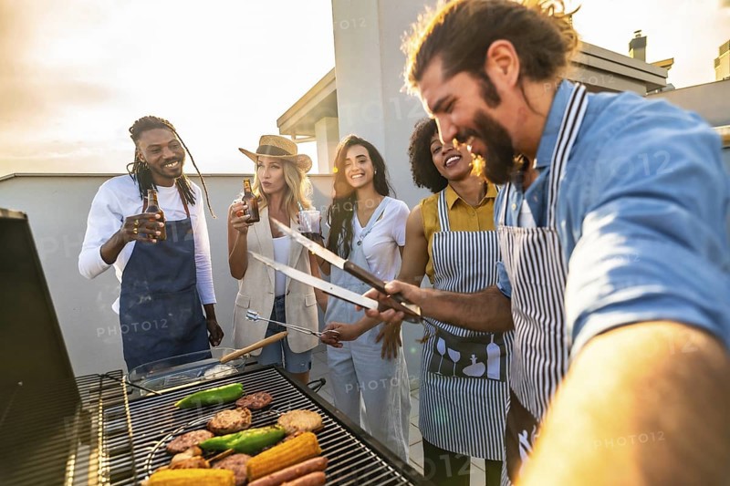 Chefs grilling food and taking a selfie on a rooftop at sunset, enjoying a barbecue party with drinks
