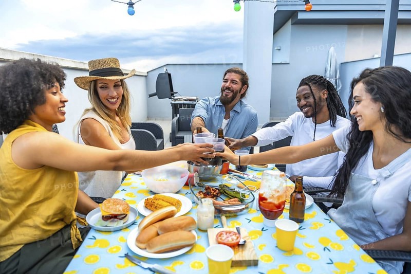 Happy multi ethnic friends toasting drinks and savoring delicious food during a lively rooftop barbecue party under the evening sky