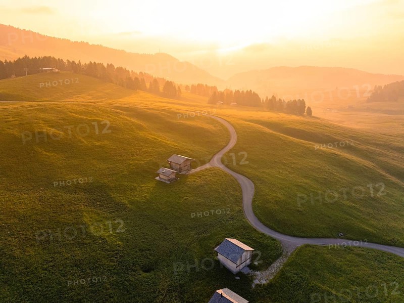 Houses on a hilly landscape at sunset, surrounded by forest, Alpe di Siusi, Dolomites, South Tyrol, Italy