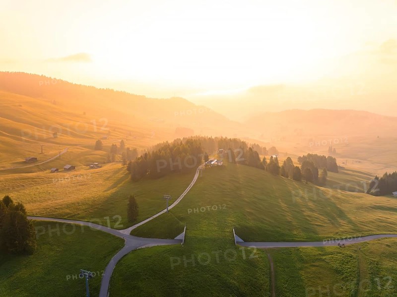 Wide, green hills under bright evening light with scattered mountain huts, Alpe di Siusi, Dolomites, South Tyrol, Italy