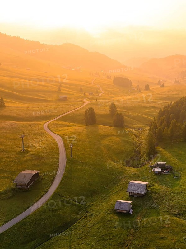 Undulating hills and forests in sunset mood with scattered mountain huts, Alpe di Siusi, Dolomites, South Tyrol, Italy