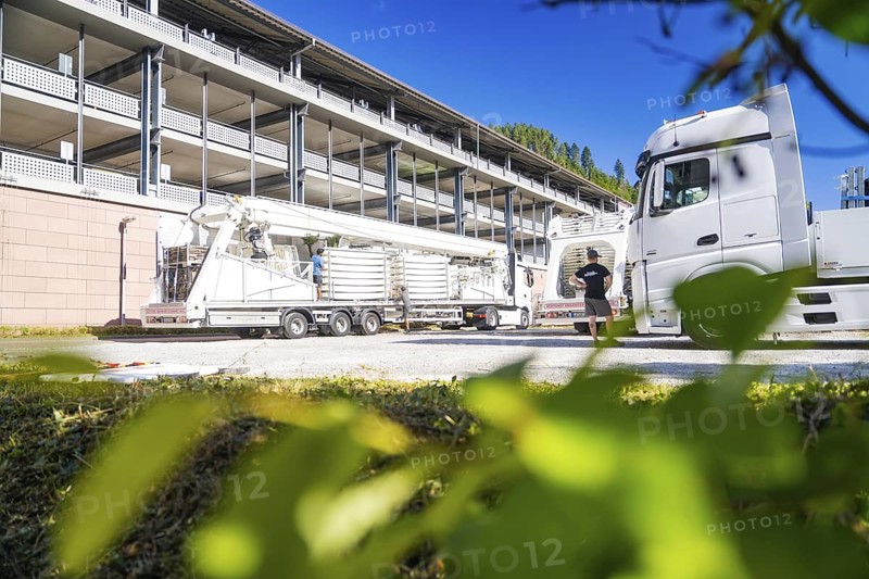 Lorry and trailer in front of a modern building, surrounded by green leaves in the foreground, Ferris wheel construction, Calw, Germany