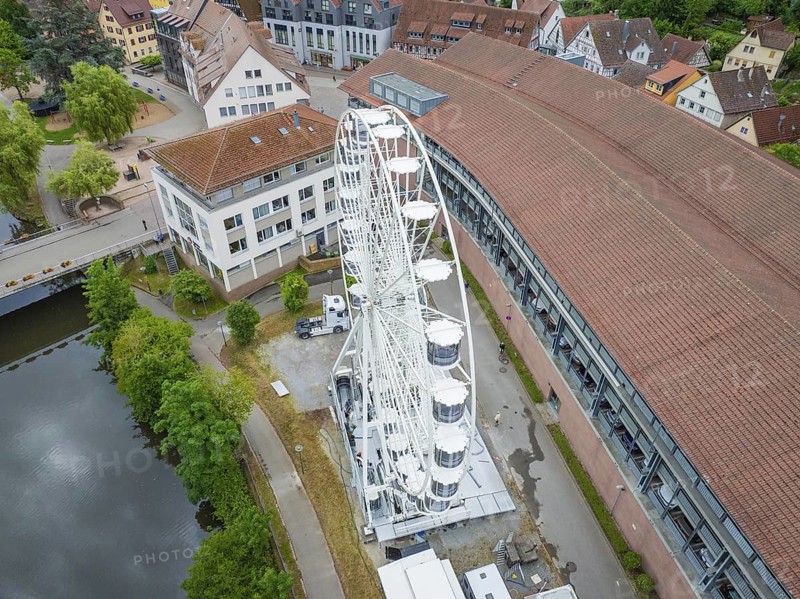 A large white Ferris wheel stands next to modern buildings with red roofs in an urban setting, Ferris wheel construction, Calw, Black Forest, Germany
