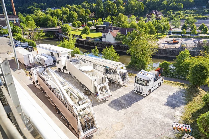 Several trucks and trailers on a car park, surrounded by green landscape and a river, Ferris wheel construction, Calw, Germany