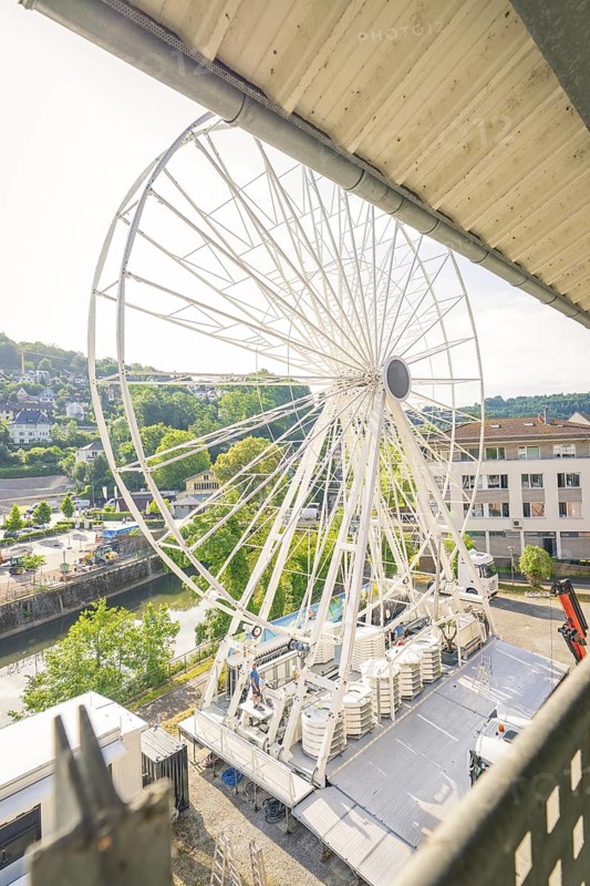 A Ferris wheel is set up in a town next to a river, surrounded by green landscape and buildings, Ferris wheel construction, Calw, Black Forest, Germany