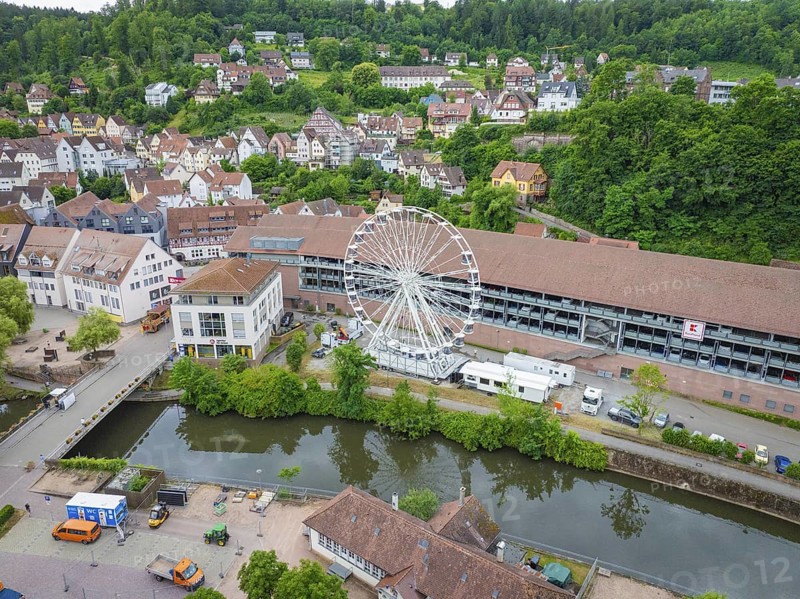 A Ferris wheel next to a river in the centre of a town with a green hilly landscape in the background, Ferris wheel construction, Calw, Black Forest, Germany