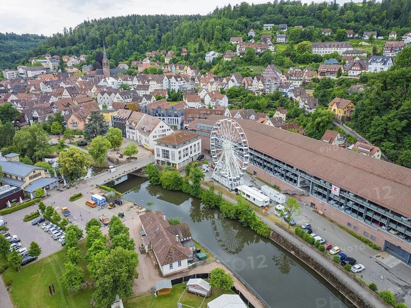 A cityscape with a Ferris wheel on a river, surrounded by a dense ensemble of buildings and hills, Ferris wheel structure, Calw, Black Forest, Germany